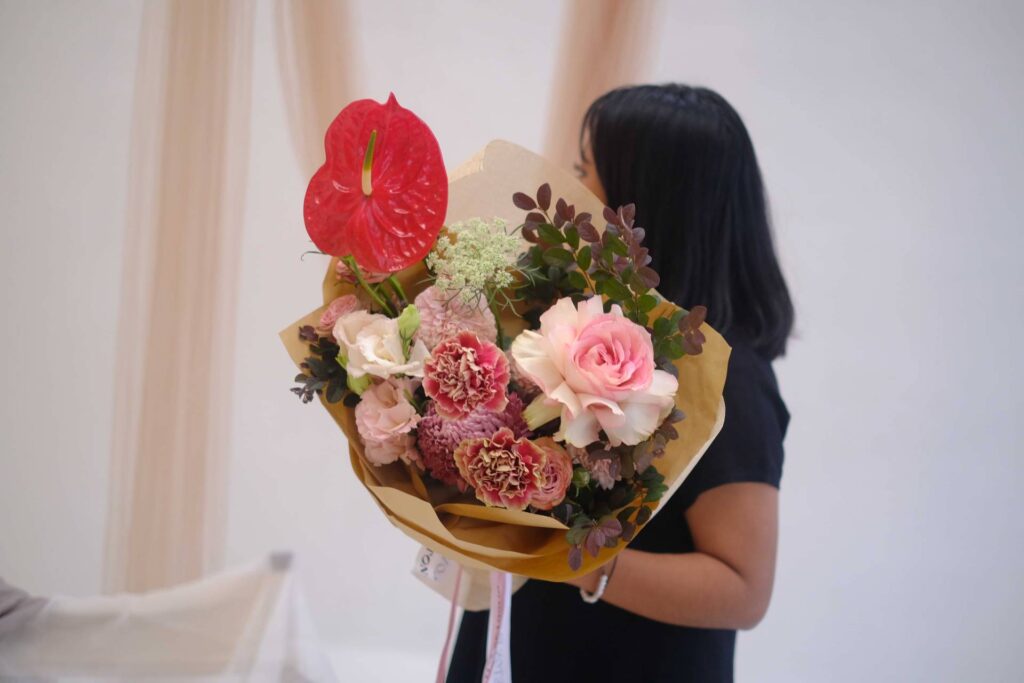 Wanita tersenyum memegang buket bunga cantik hasil karya Flowerchef dengan paduan warna pastel